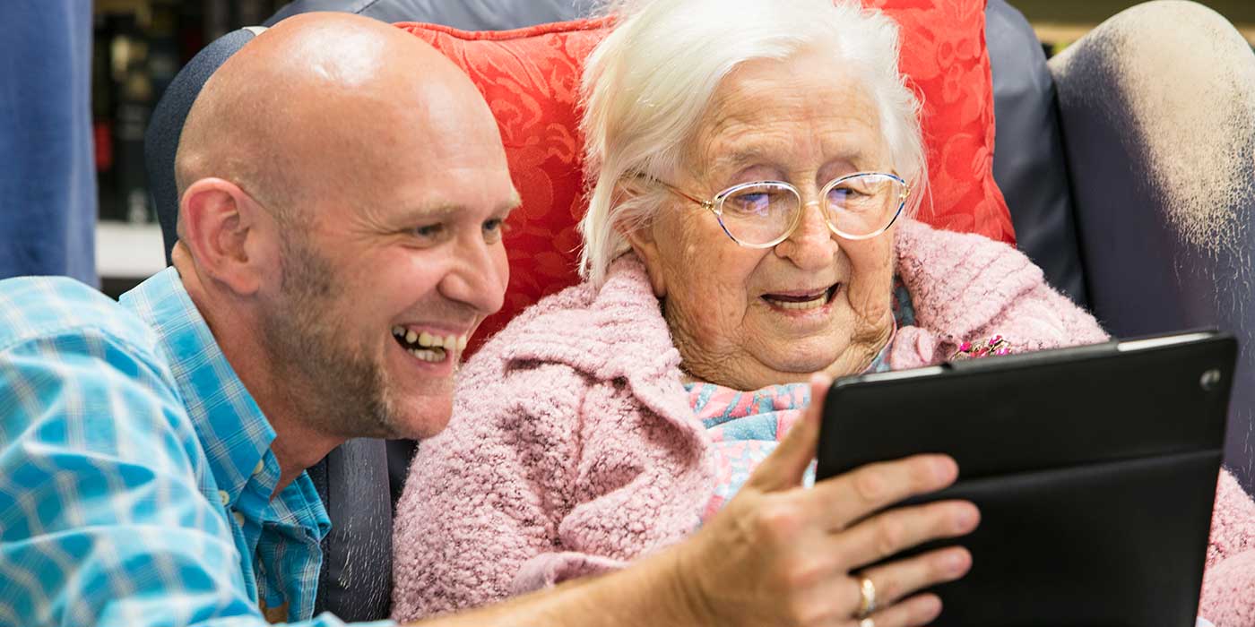 A Whiddon carer laughing along with a resident as they play on an iPad at a community care home in Maitland.