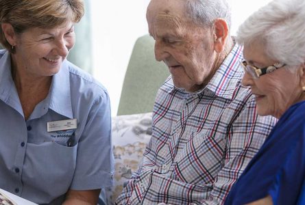 A Whiddon carer enjoying a book with two residents at Whiddon's Belmont nursing home.