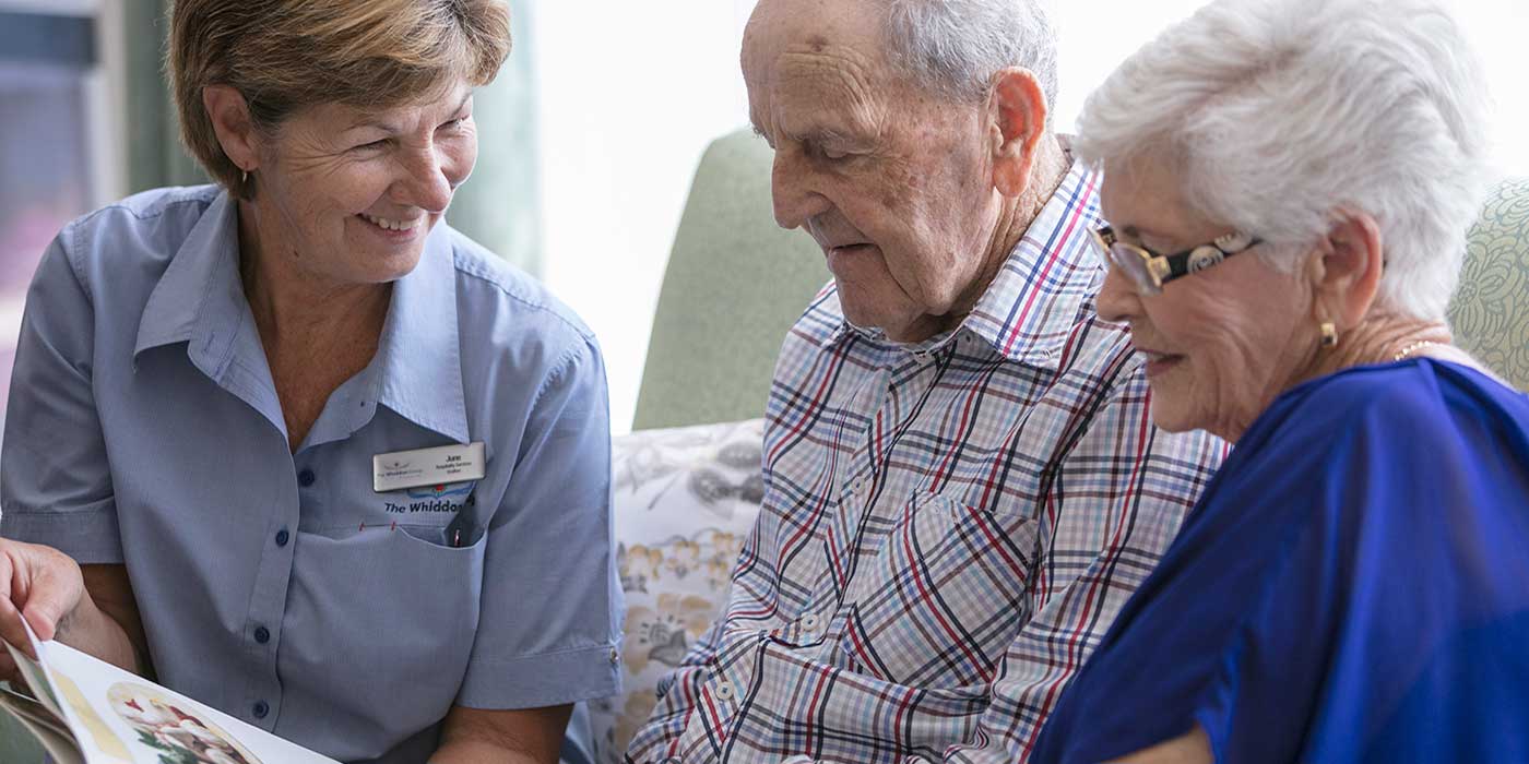 A Whiddon carer enjoying a book with two residents at Whiddon's Belmont nursing home.